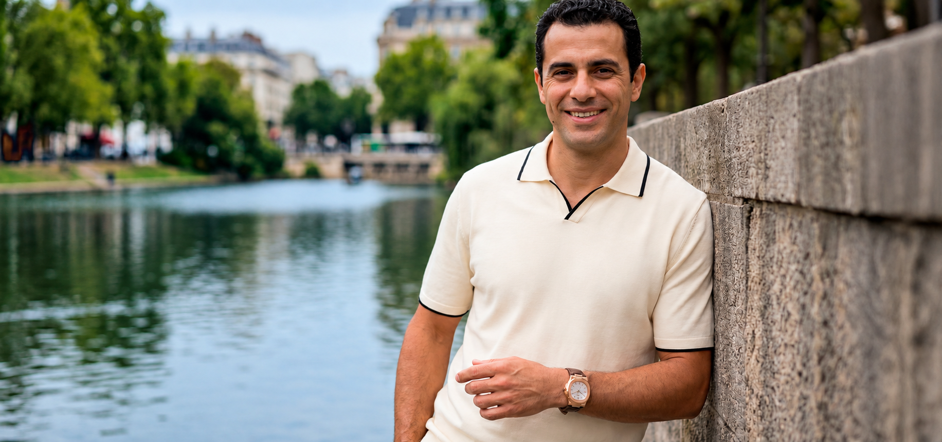 Hombre con polo claro junto a un lago, en un entorno urbano